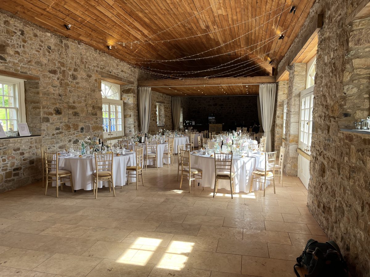 Colstoun House barn wedding reception venue dressed with white linen round tables, gold chiavari chairs, fairy lights and stone walls, East Lothian