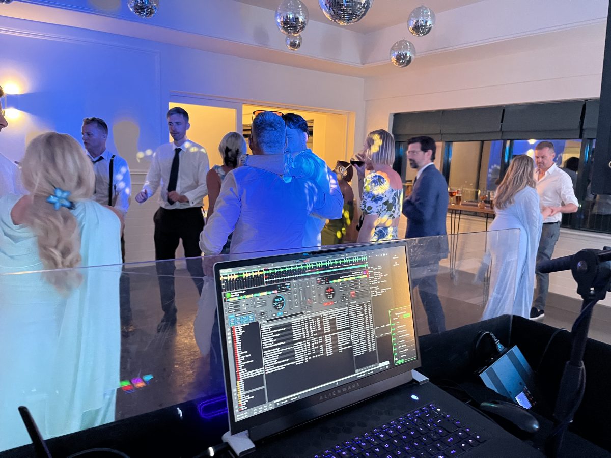 Behind the DJ booth at Whitekirk Hill — Alienware laptop running Virtual DJ with guests dancing behind