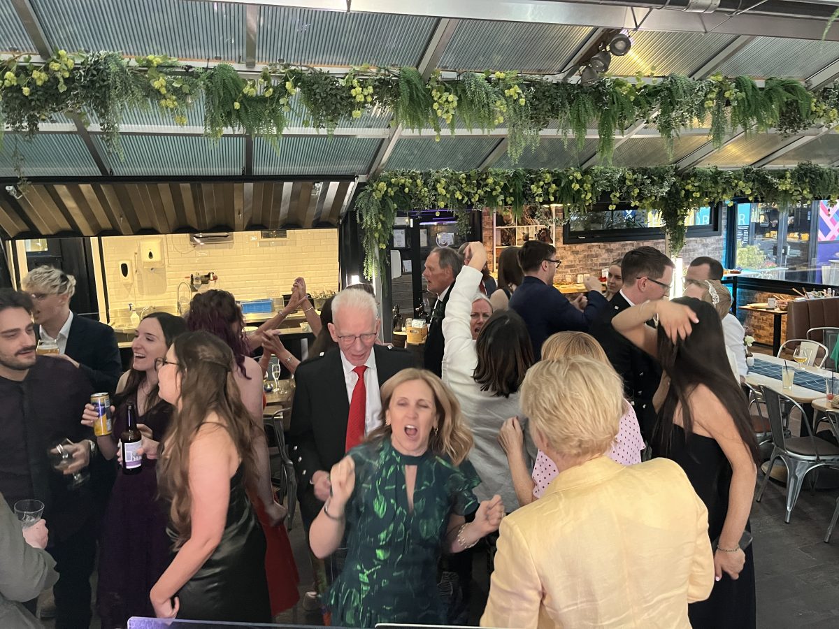 Packed dancefloor at Stewart Brewing wedding with guests celebrating under hanging greenery