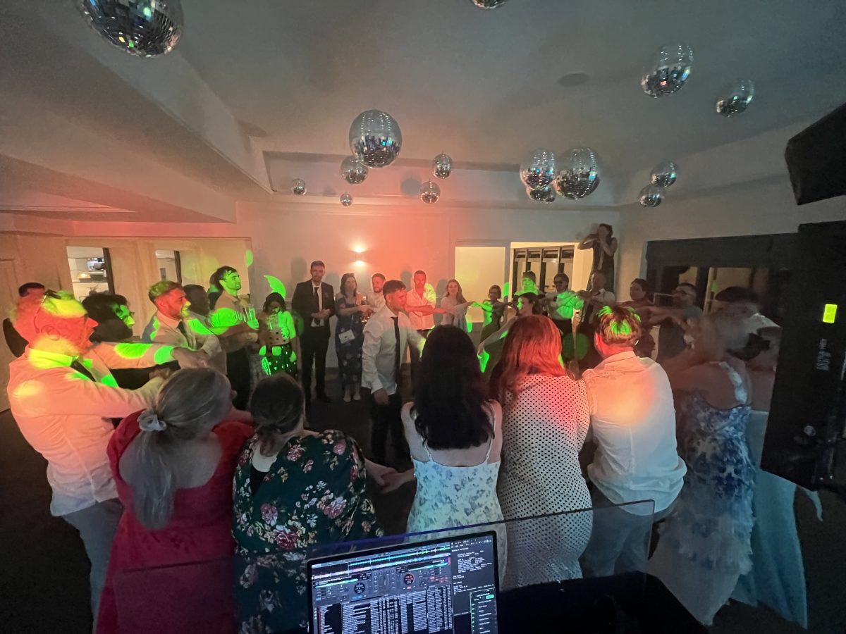 DJ view over laptop of packed Whitekirk Hill wedding dancefloor under green and orange lighting